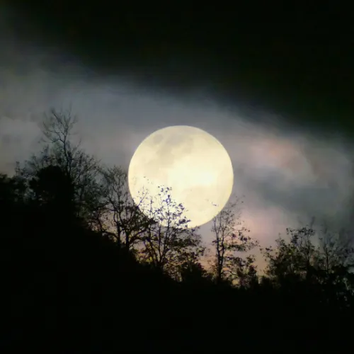 Eerie full moon rising over a hill 